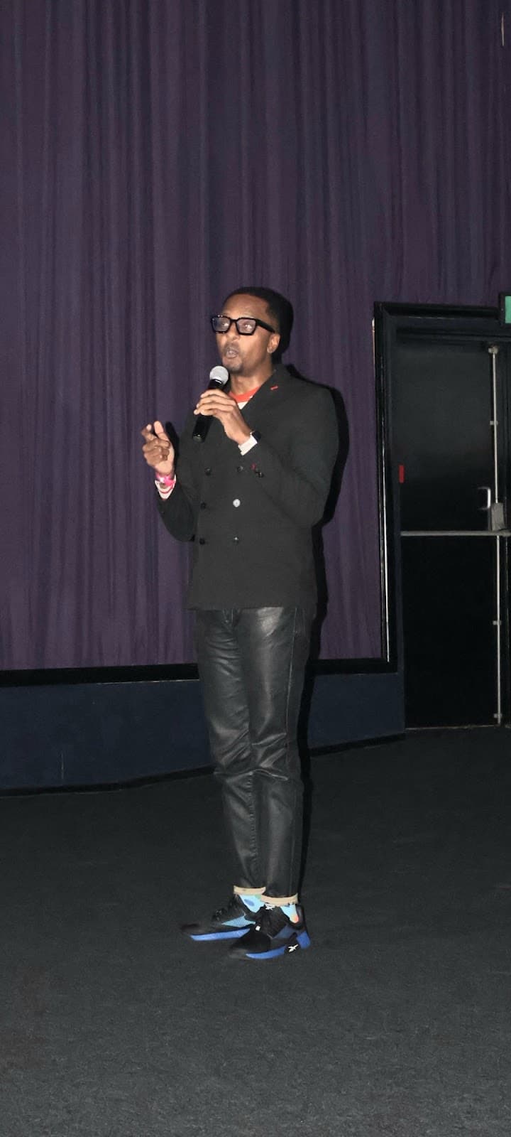 A speaker holds a microphone in front of the cinema curtains.