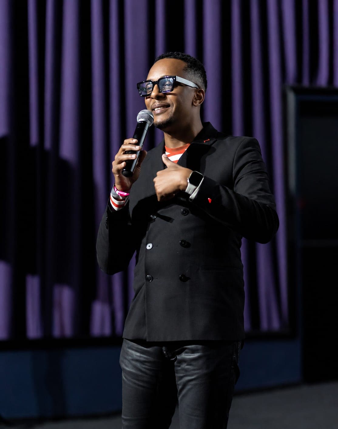 A speaker holds a microphone in front of cinema curtains.