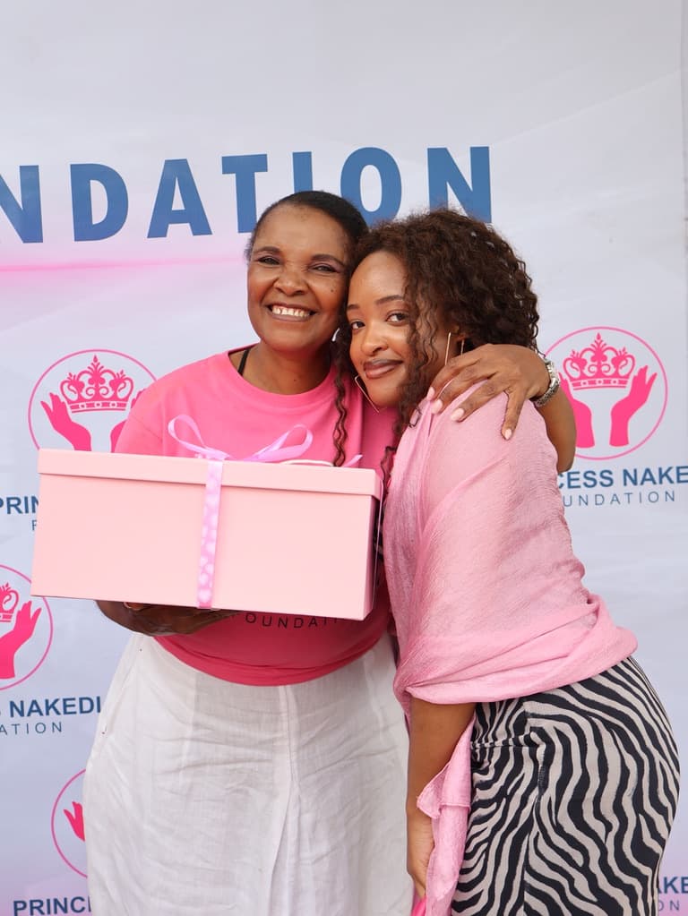 Princess Nakedi and a community member embrace while holding a pink gift box